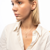 A woman wearing a white shirt, showcasing a sterling silver safety pin necklace with a beaded satellite chain.